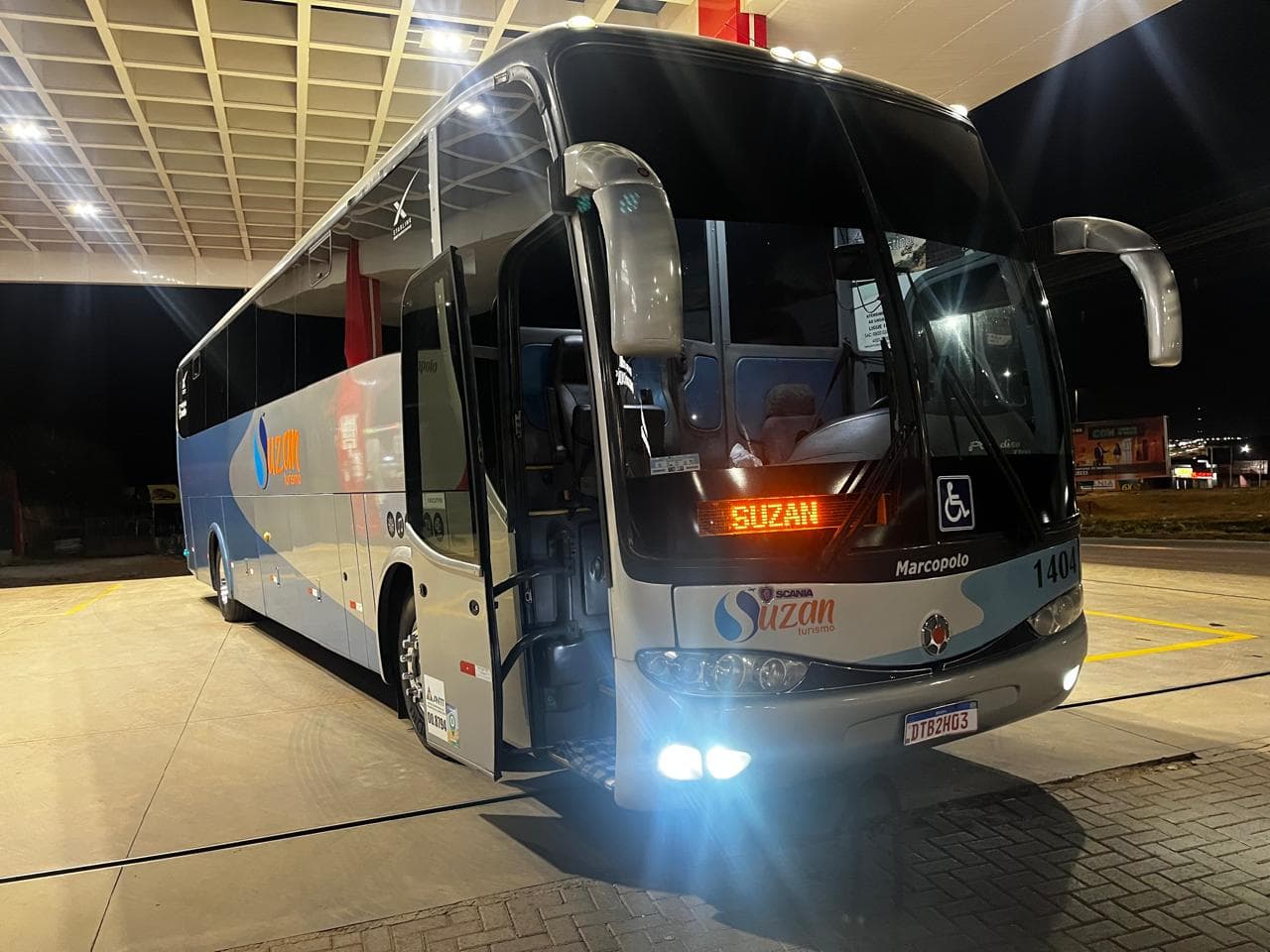 Ônibus da Suzan Turismo à noite, com a porta aberta e o letreiro SUZAN aceso