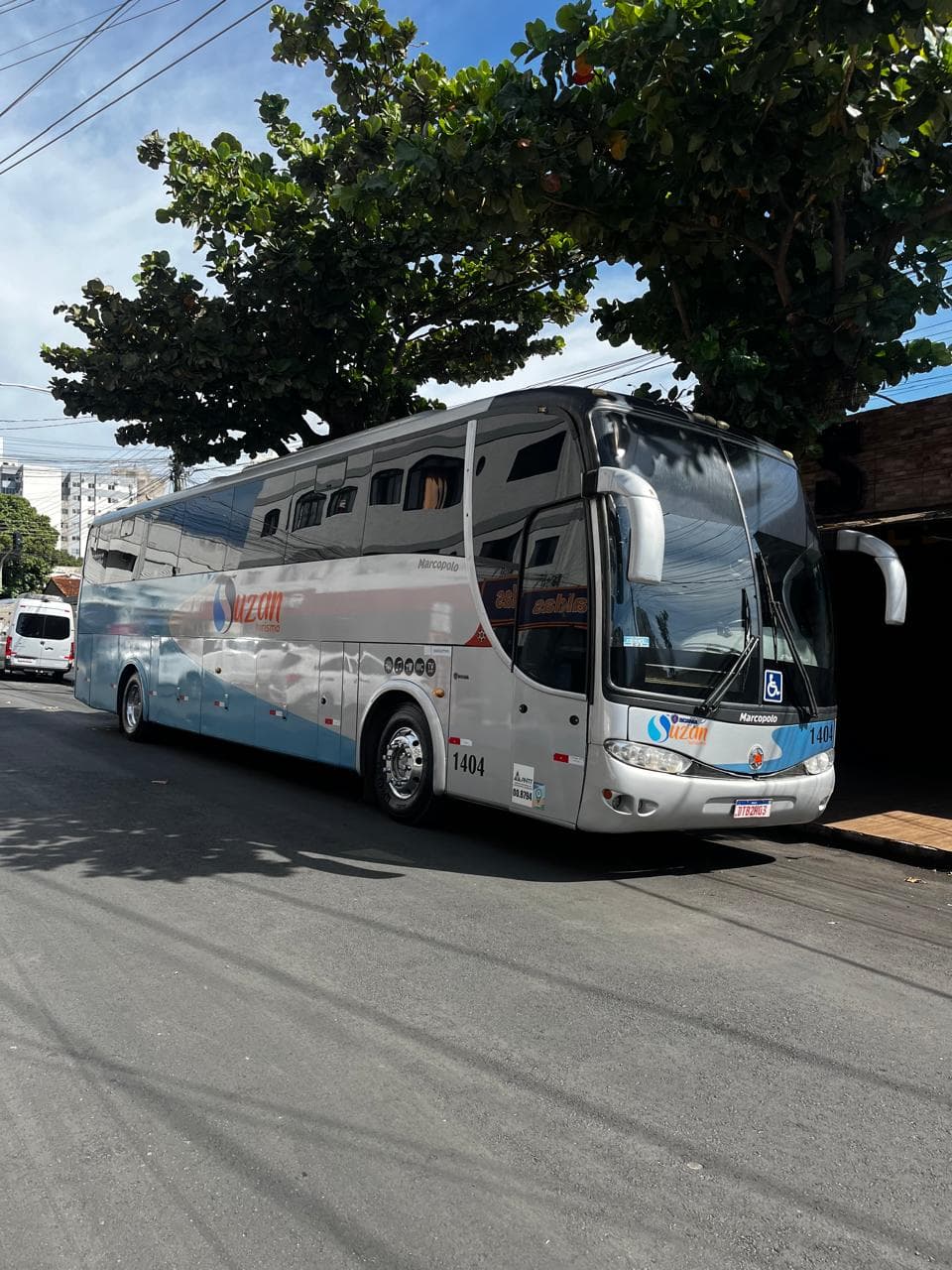 Ônibus da Suzan Turismo estacionado na rua sob árvores
